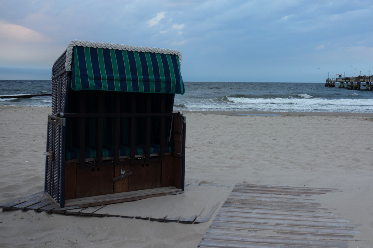 Koserower Strand. Zentral ein Strandkorb, der auf einem Holzsteg steht im Hintergrund das Meer.
