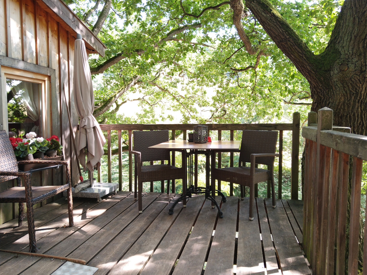 Holz-Terrasse mit einem Tisch und 3 Stühlen sowie einem Sonnen-Schirm.