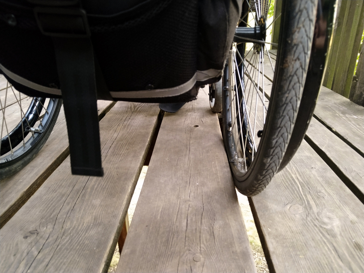 Rollstuhl, bei dem ein Reifen in einer Spalte zwischen 2 Brettern festhängt.