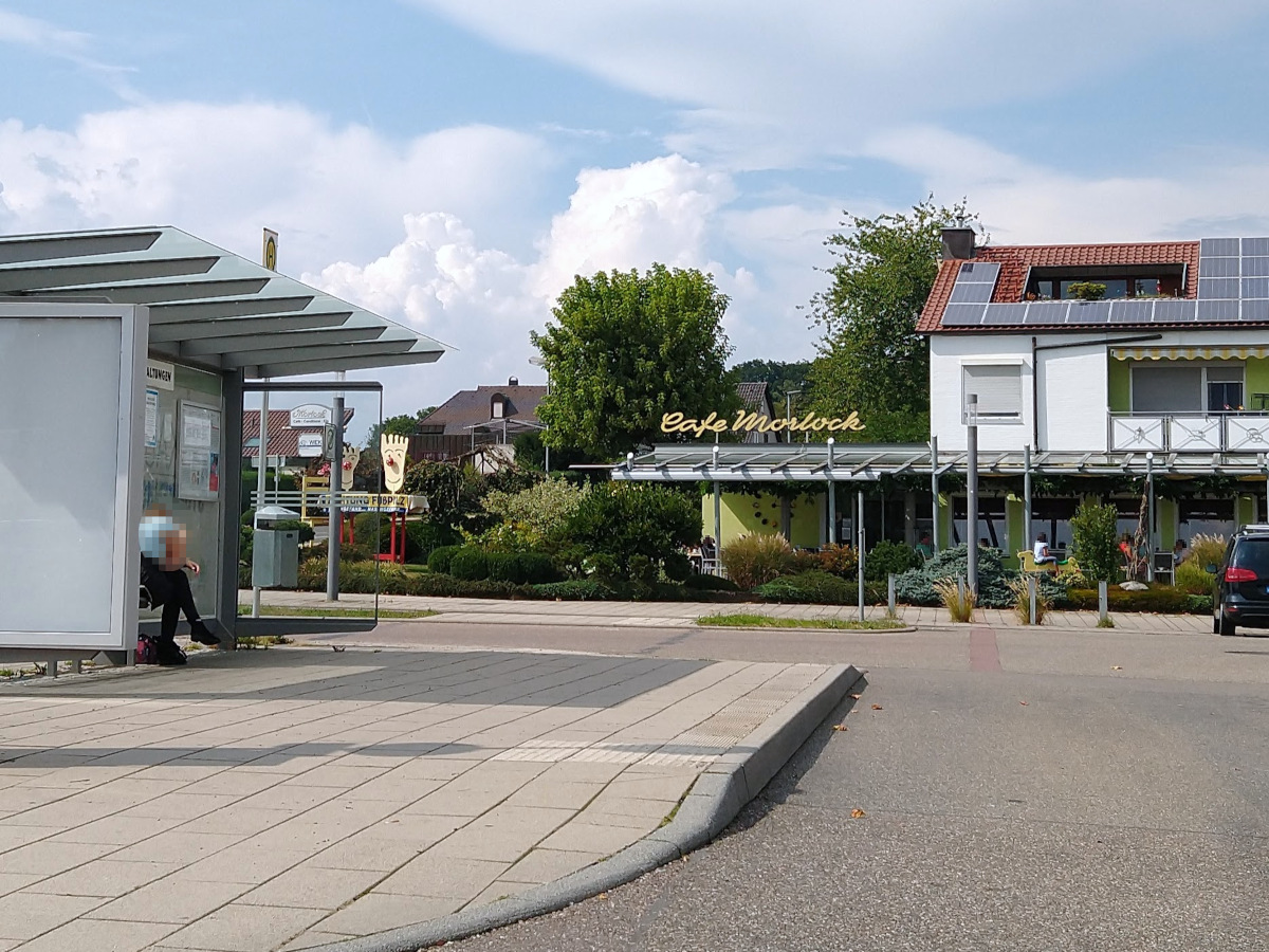 Bus-Haltestelle im Vordergrund. Im Hintergrund das Café Morlock. Bus-Halte-Stelle mit erhöhtem Bordstein und Blinden-Aufmerksamkeits-Feld.