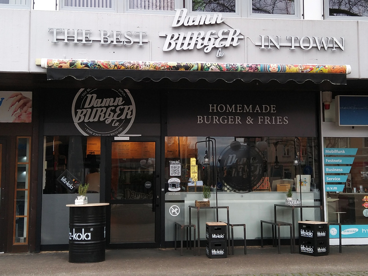 Außen-Ansicht von Damn Burger. Restaurant im Erd-Geschoss. Glas-Front mit Glas-Tür.