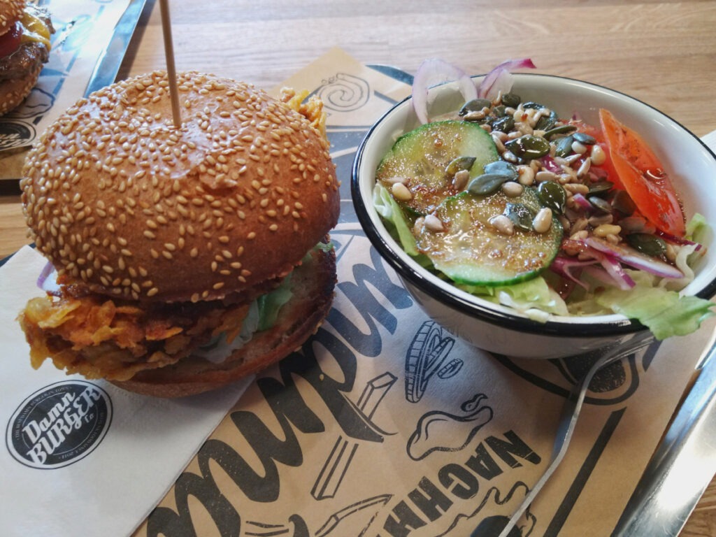 Burger mit knusprig paniertem Patty in Cornflakeskruste und daneben eine Schale Salat.