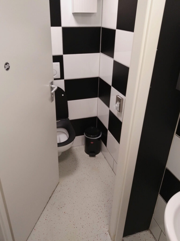 Blick durch eine halb geöffnete Tür in eine kompakte Toilette. Die Tür öffnet nach innen.