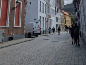 Stadtstraße mit schmalen Gehwegen auf beiden Seiten. Auf dem rechten Gehweg gehen zwei Personen hintereinander, die aufgrund der Enge nicht überholen können.