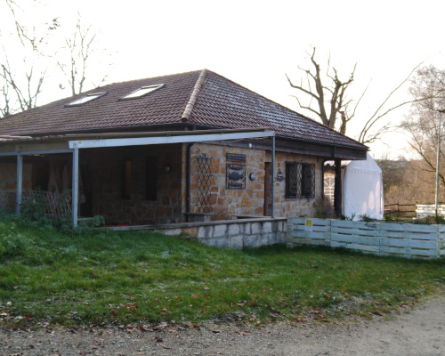 Fischerhütte von außen. Rustikales, einstöckiges Haus aus Naturstein mit weißem Zaun aus Euro-Paletten.