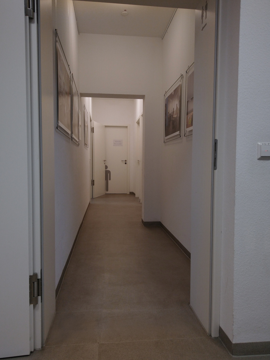 Länger Flur. Am Ende die Herren-Toilette. Davor rechts die Damen-Toilette und links die Tür zum linken Gebäude-Teil.