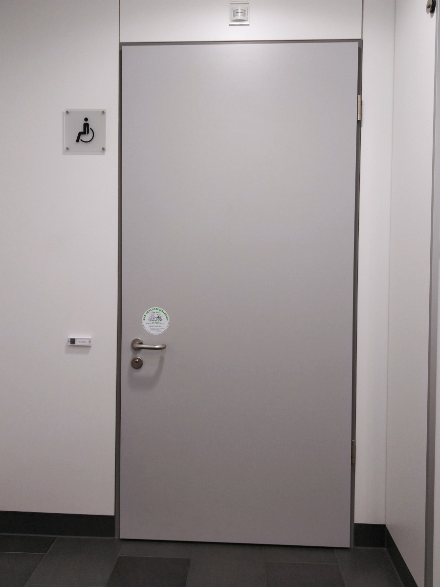 Tür zur Behinderten-Toilette. Niedriger Tür-Griff. Aufkleber mit dem Hinweis auf den Zugang über einen Euro-Schlüssel.