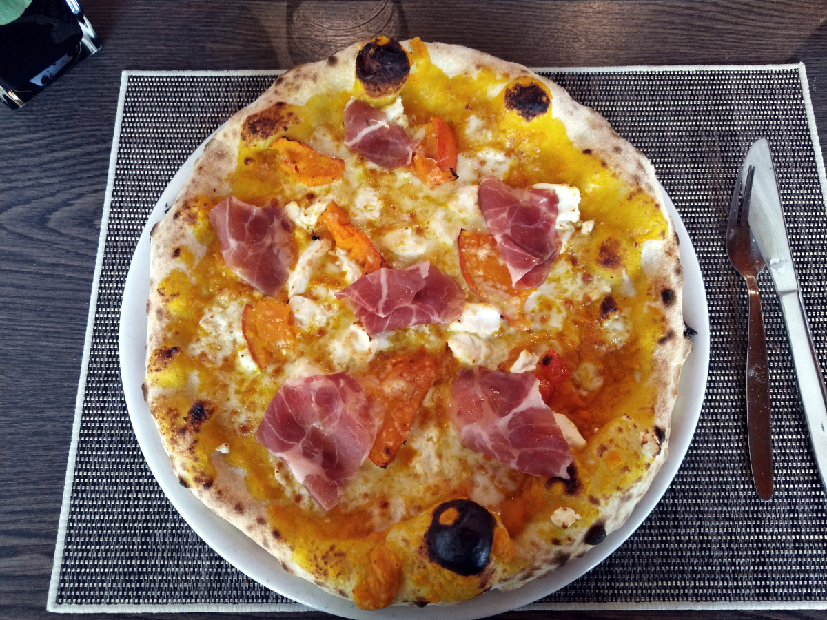 Pizza mit Kürbis und luftgetrocknetem Schinken auf Ziegenfrischkäse. Duch den Kürbis Pizza sehr orange.