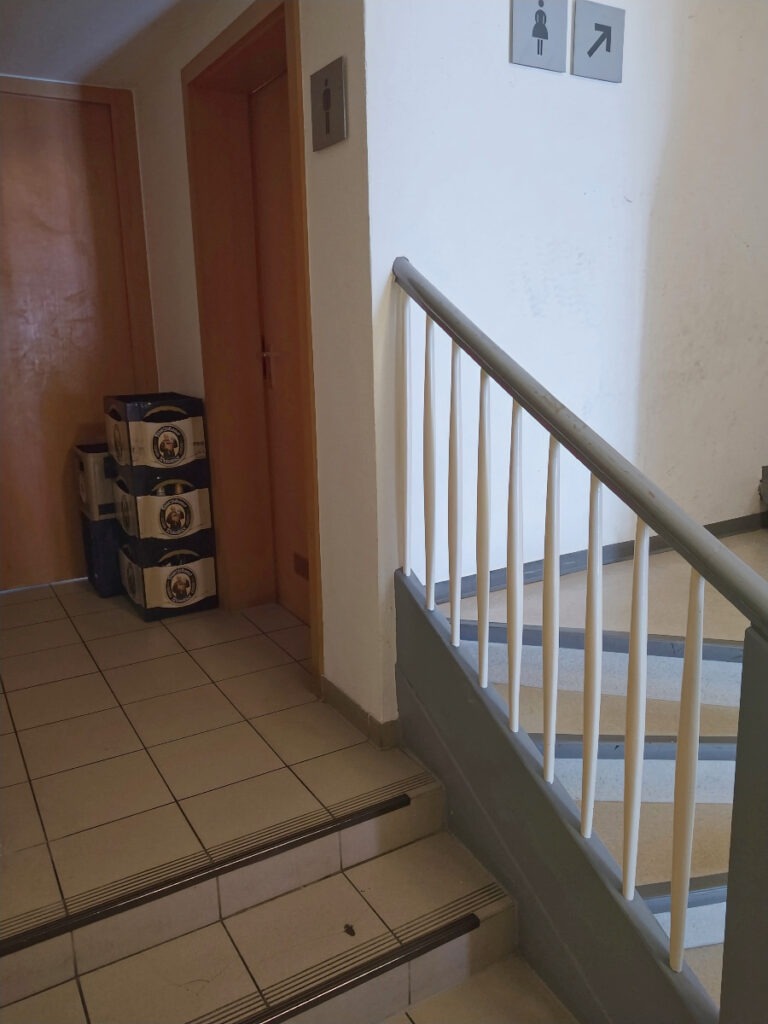 Neben der Treppe im Treppenhaus befinden sich drei separate Stufen, die zu einer Tür mit einem Herrentoiletten-Schild führen.