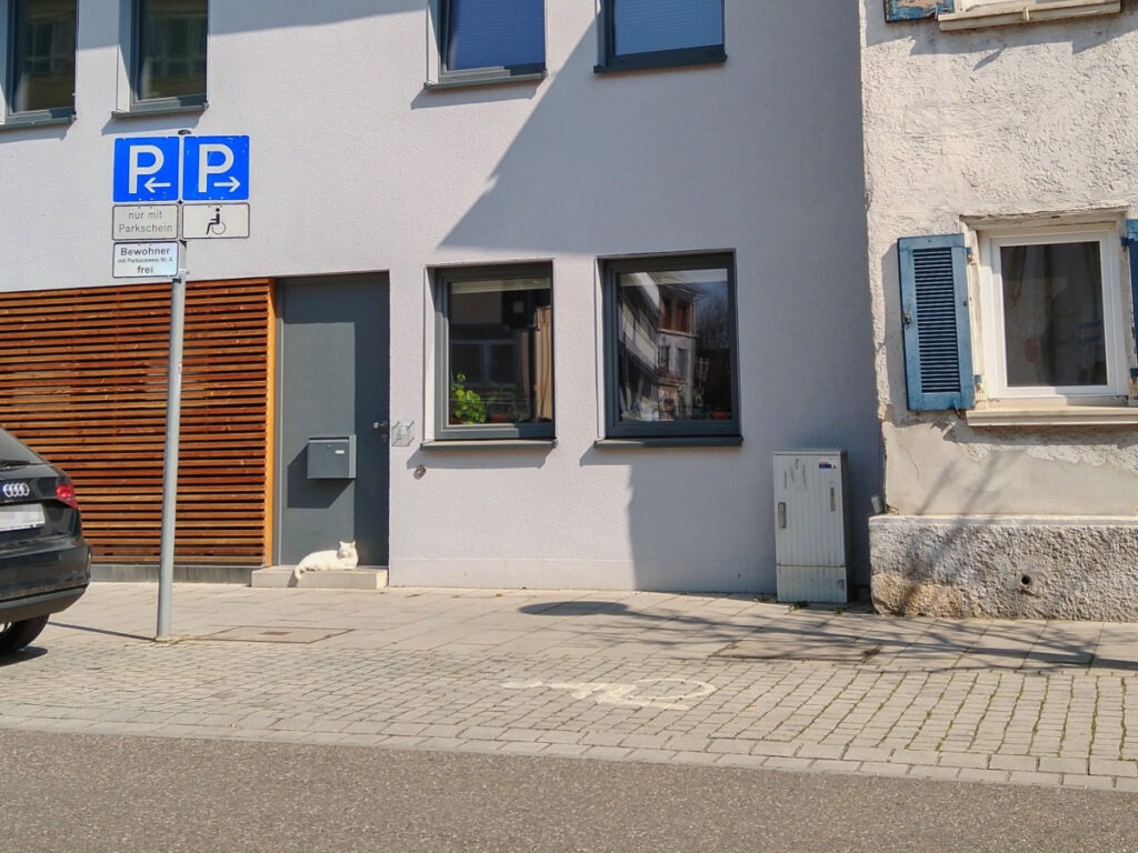 Ein Behindertenparkplatz mit Schild und Bodenmarkierung vor einem Haus.