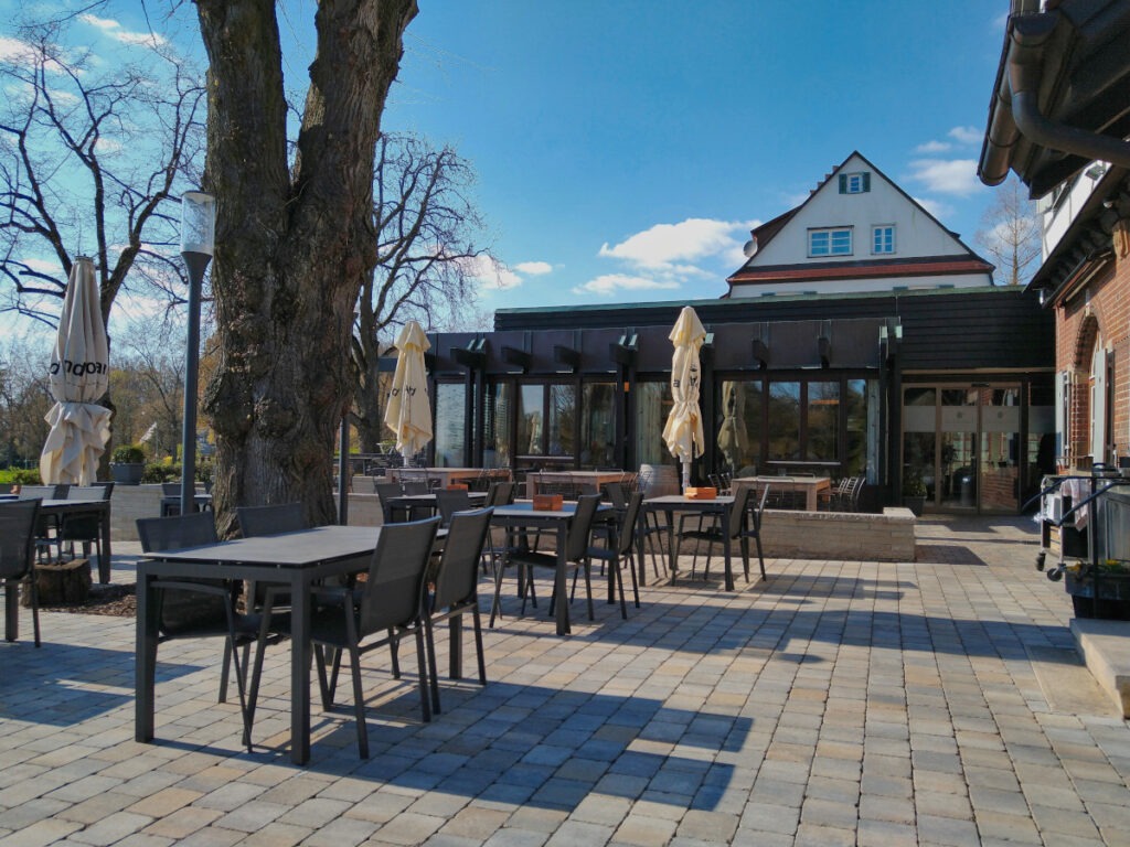 Gepflasterte Außenterrasse mit mehreren Tischen und Stühlen, im Hintergrund das Restaurant.