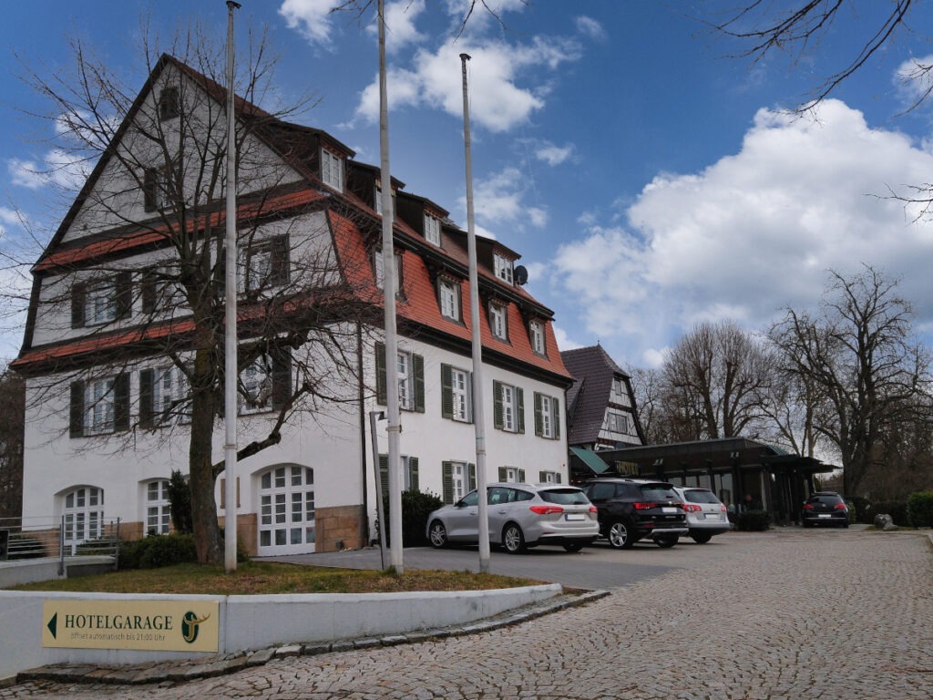 Gepflasterte Einfahrt zum Hotel Jägerhaus mit mehreren vor dem Gebäude geparkten Autos.