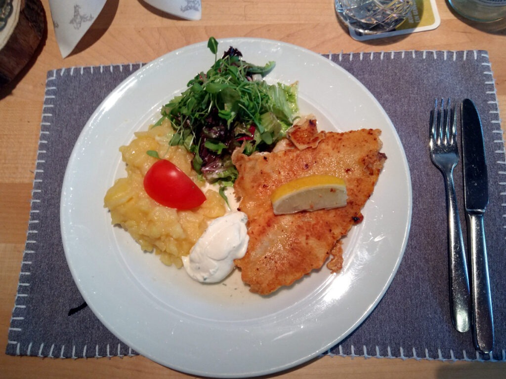 Teller mit Kartoffelsalat, paniertem Fisch, Remoulade und Blattsalat.