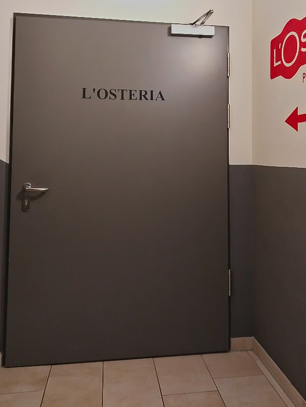 Metalltür mit dem Schriftzug „L'Osteria“ am Eingangsbereich des Restaurants.