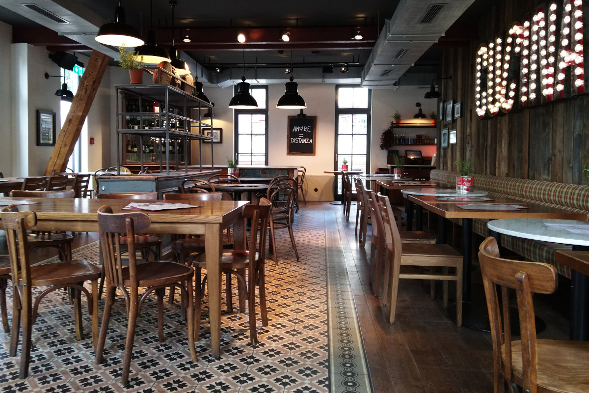 Innenbereich des Restaurants L'Osteria mit rustikalen Tischen und Stühlen