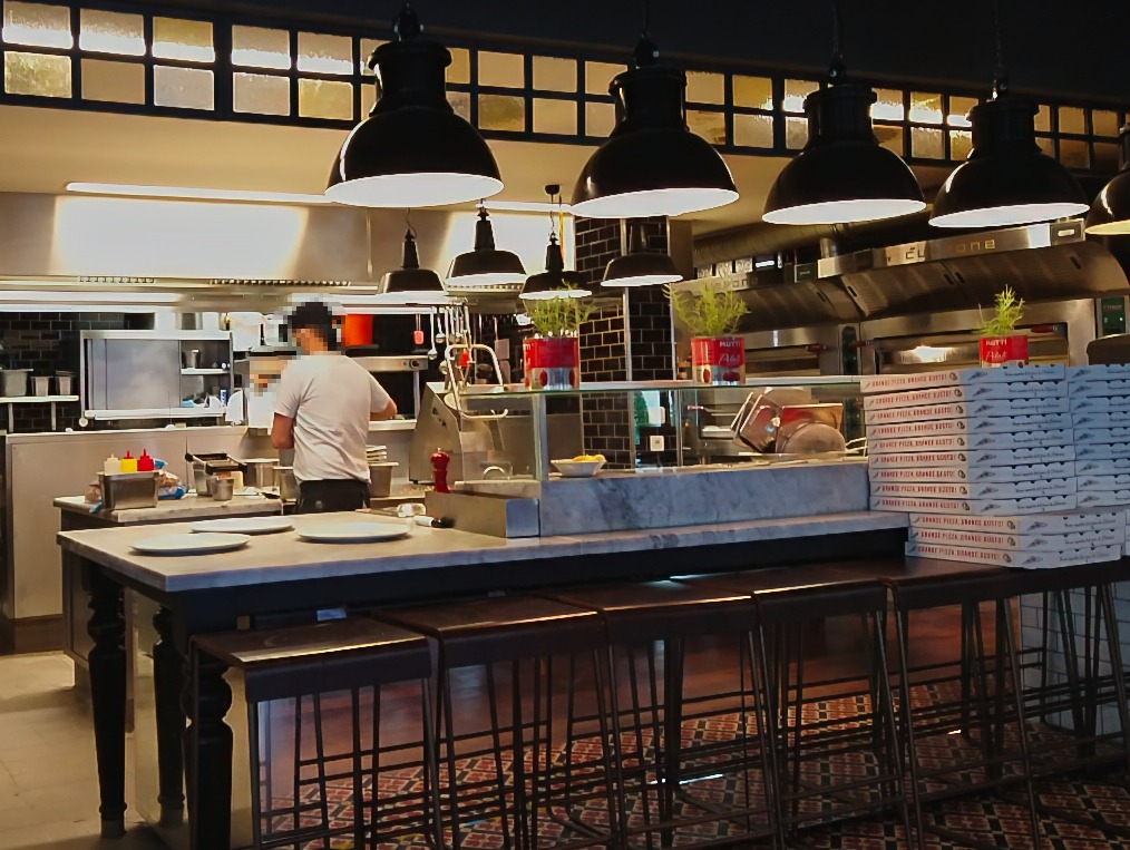 Blick in die Küche, ein Mitarbeiter bereitet mit dem Rücken zur Kamera Zutaten für Pizza vor.