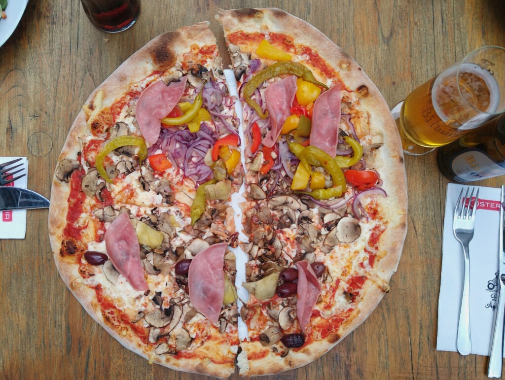 Pizza in der Mitte durchgeschnitten, beide Hälften mit jeweils zwei unterschiedlichen Belägen.
