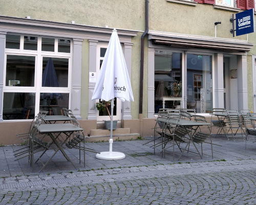 Restaurant "La Galette" von außen. Im Vordergrund Tische und Stühle. Im Hintergrund das Restaurant mit seiner Glasfront.