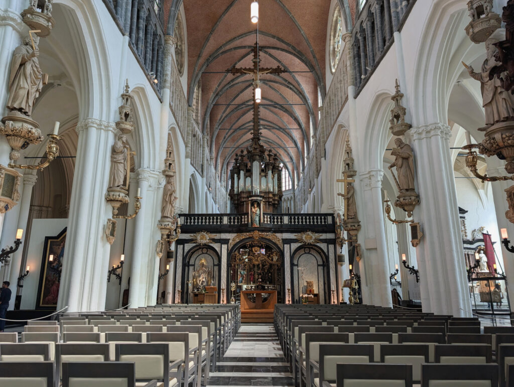 Weißes Kirchenschiff mit Stuhlreihen vor dem Altar, darüber eine Orgel, an den Säulen links und rechts erhöhte weiße Statuen.