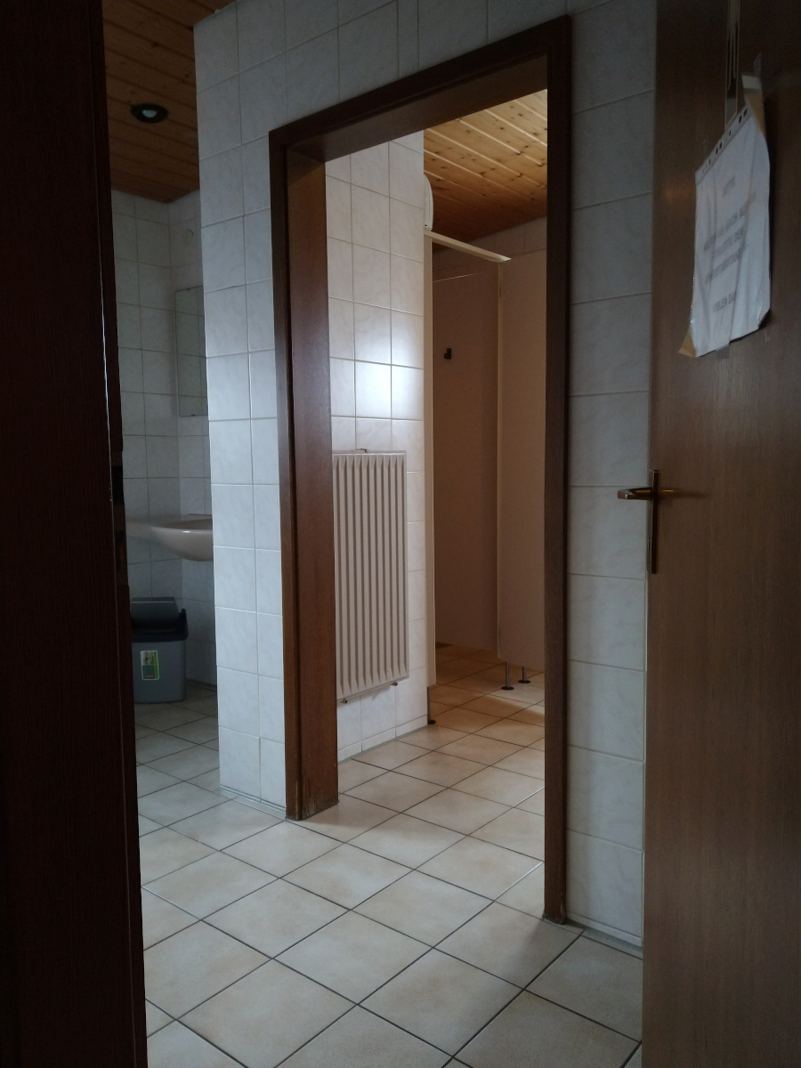 Zugang zur Herren-Toilette. Vorraum mit Waschbecken. Schräg links von der Eingangs-Tür Durchgang zu den Toiletten.