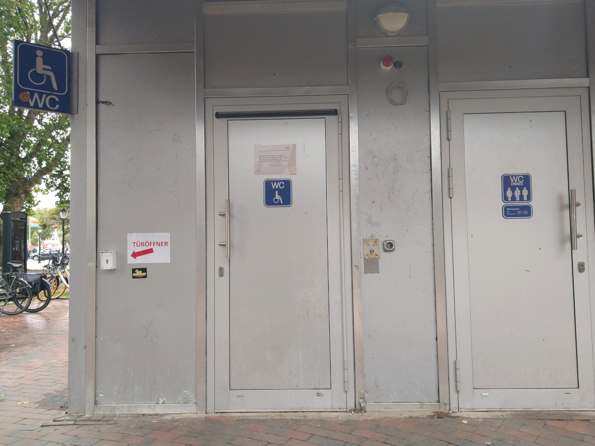 Links eine Tür zu einer Behinderten-Toilette, rechts eine Tür zu einer Unisex-Toilette.