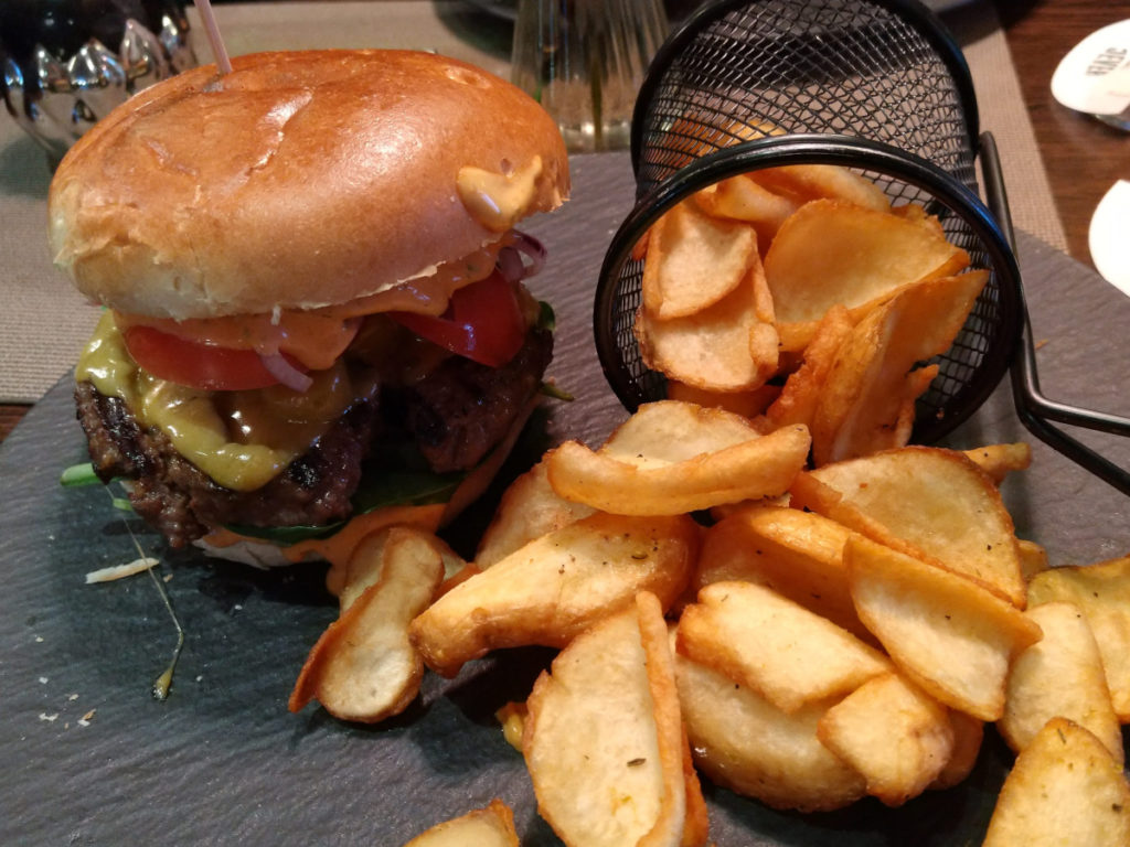 Schiefer-Platte auf der ein dick belegter Burger und eine Portion breite Kartoffel-Chips liegen.