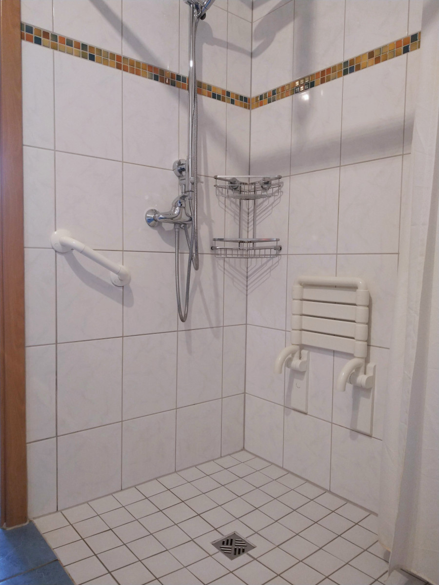 Stufenlos zugängliche Dusche mit Klappsitz und Dusch-Vorhang.