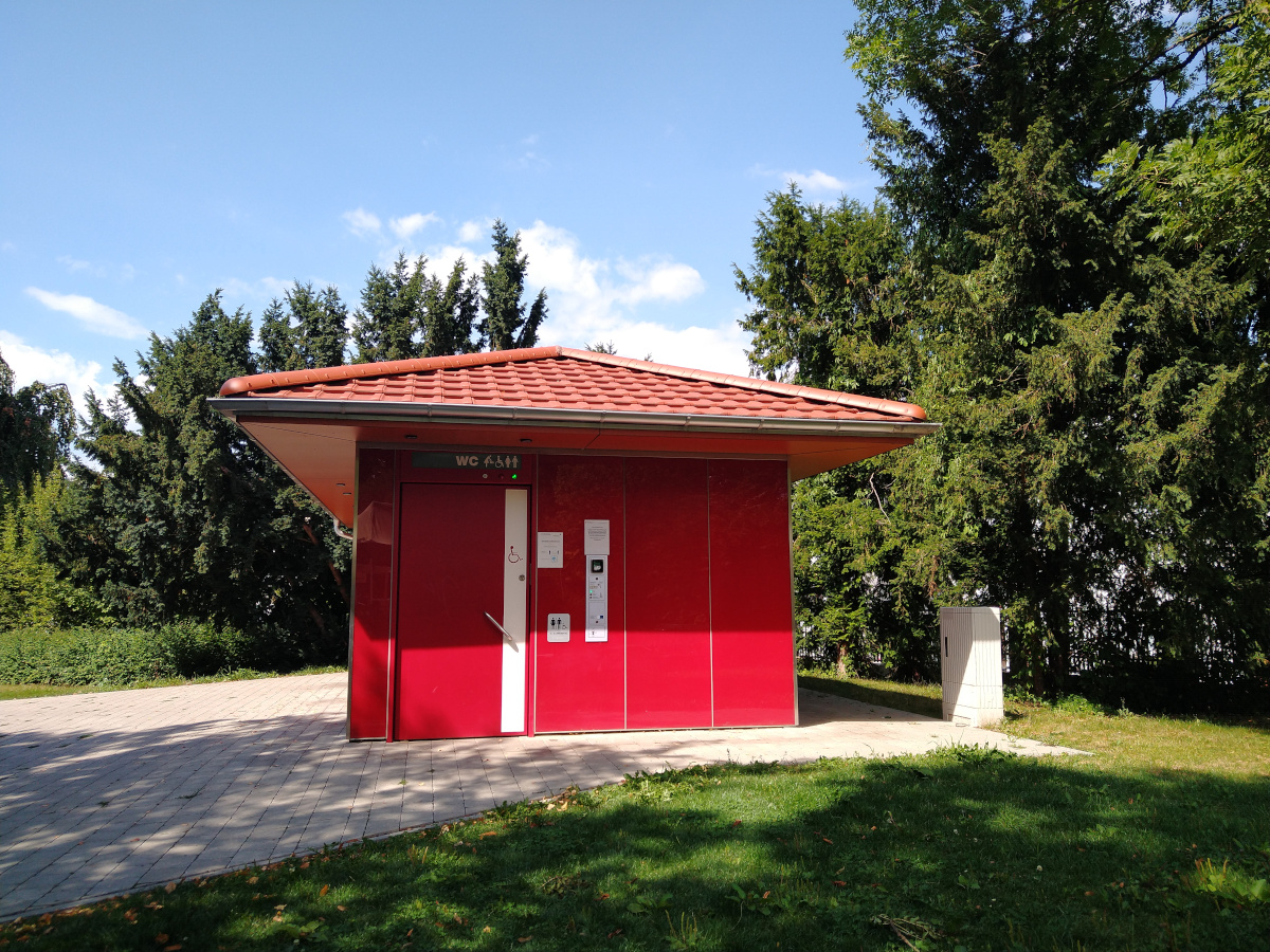 Öffentliche Toilette im Park. Rotes Gebäude. Behinderten-Toilette vorhanden.