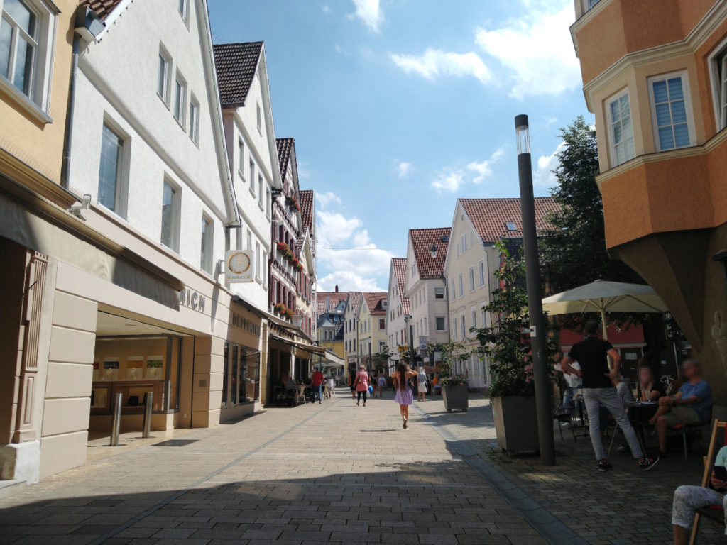 Gepflasterte Fußgänger-Zone mit Geschäften und Cafés.