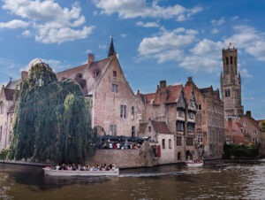 Kanal mit flachem Boot voller Menschen, im Hintergrund hohe historische gemauerte Gebäude, rechts hinten ein gemauerter Turm.
