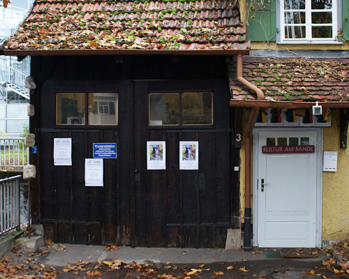 Außenansicht der "Alten Spinnerei". Links eine Garage mit 2-flügligem Holztor. Rechts kleines gelbes Häuschen.