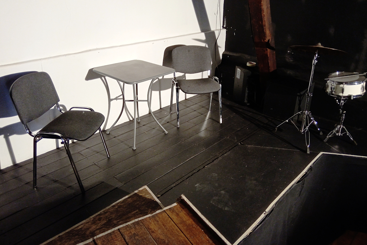 Blick auf die kleine Bühne. Auf der Bühne ein Tisch mit 2 Stühlen.