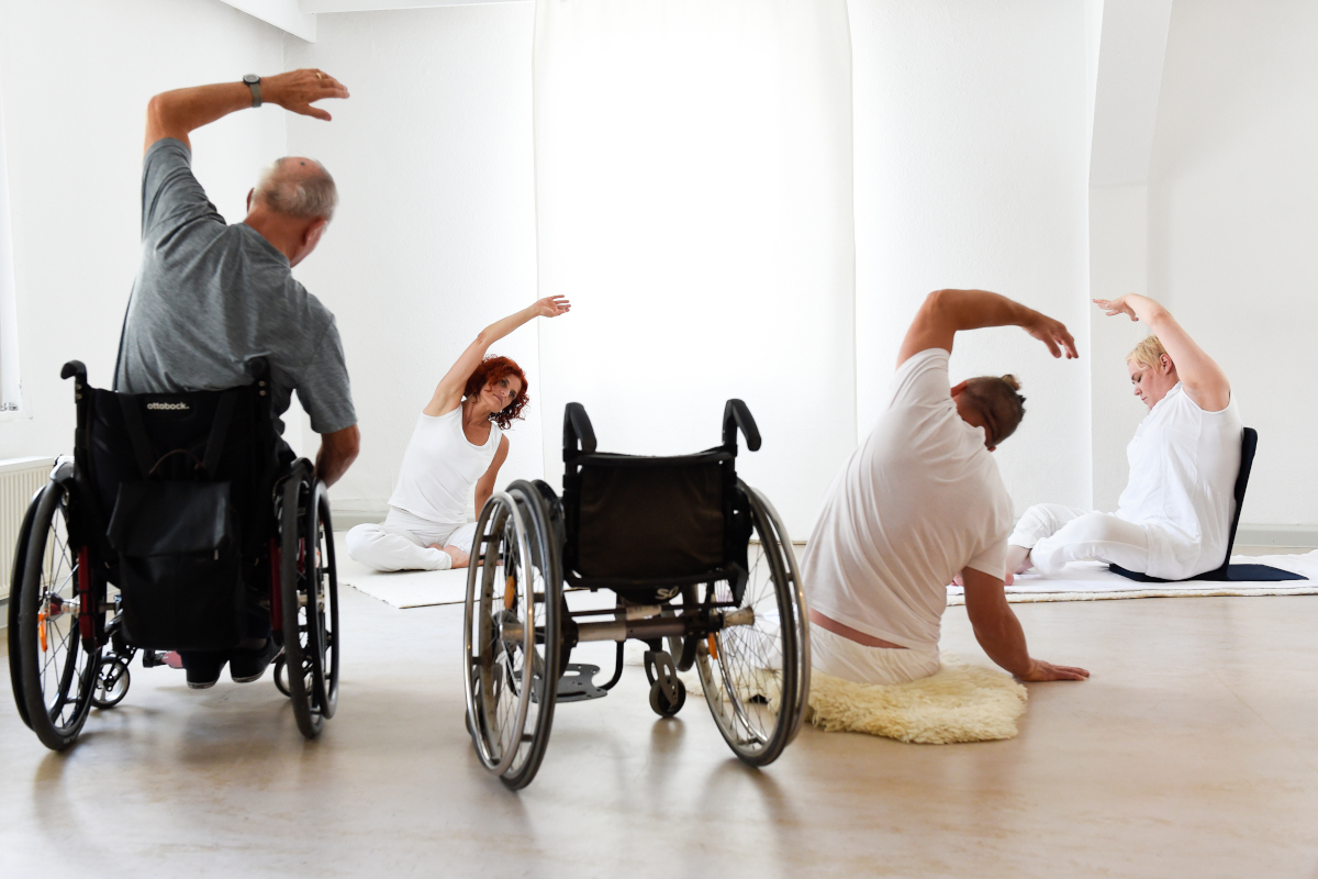 Yogagruppe mit zwei Rollstuhlfahrern und eine Rollstuhlfahrerin